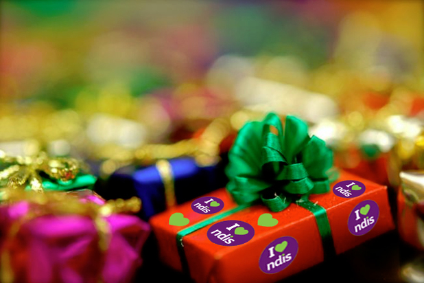 A stack of brightly wrapped presents - the top present has a green bow and the words 'I love NDIS' on it. 